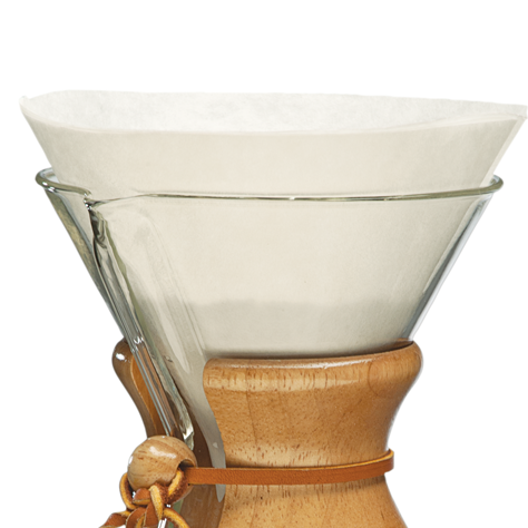 Clear glass coffee dripper with wooden base and white filter on a white background